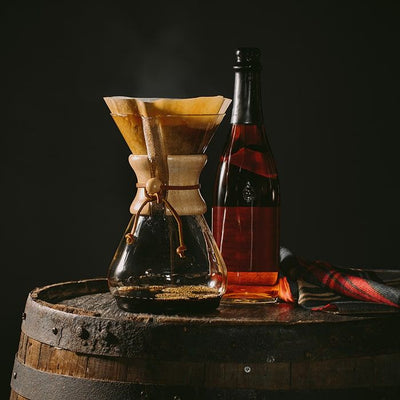 Coffee Bean Direct Highlander Grogg -- pourover alongside bottle of liquor resting on a barrel