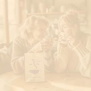 Mother's Day and Gift Subscriptions featured mobile hero with beige overlay -- mother and daughter sitting at kitchen table having a cup of Coffee Bean Direct coffee
