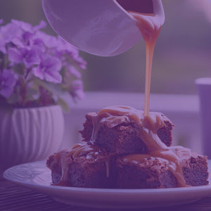 Salted Caramel Brownie featured mobile hero -- brownies with caramel sauce on a plate with a purple mug and flower pot in the background