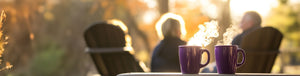 Grandfather's Blend Sale featured hero -- Two purple mugs with steam on a table outdoors with two people sitting in the background