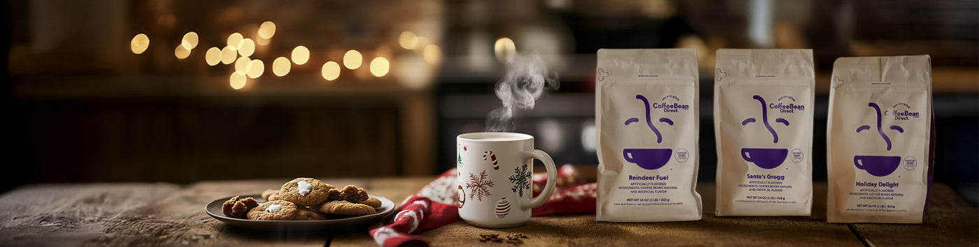 Holiday Gift Bundles featured hero -- Trio of Coffee Bean Direct holiday coffee bags alongside mug of hot coffee and cookies in a Christmas setting