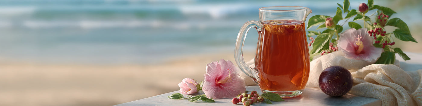 Passion Punch Black Tea featured hero -- pitcher of iced black tea on a table alongside hibiscus flowers and berries with a beach in the background