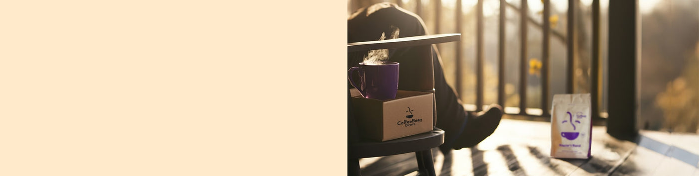 Roaster's Blend Subscription featured hero -- person sitting on porch alongside Coffee Bean Direct delivery box, purple mug filled with coffee, and Roaster's Blend bag