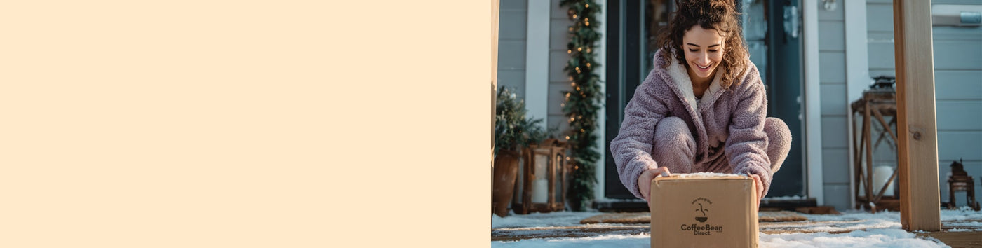 10% Subscription Discount Upgrade featured hero -- Woman in a winter coat picking up a Coffee Bean Direct delivery box on a snowy porch