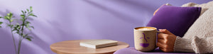 Subscription landing page hero -- person holding a branded coffee mug with a latte and a coffee table with a book in the background