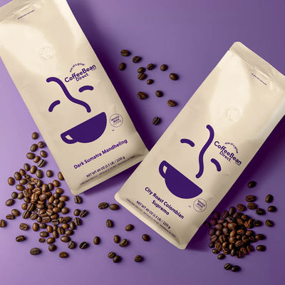 Coffee Bean Direct Single Origin Dark and Medium Subscription -- Dark Sumatra Mandheling and City Roast Colombian Supremo coffee bags alongside piles of fresh roasted coffee beans