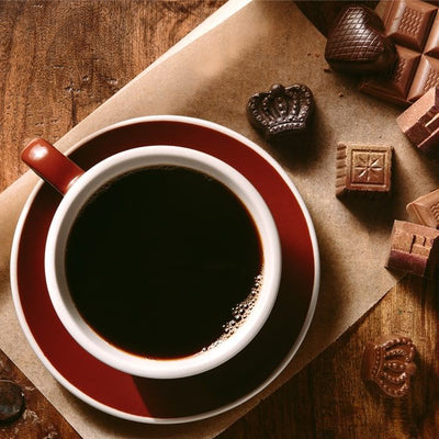 Coffee Bean Direct Decaf Chocolate flavored coffee -- coffee mug on dish alongside assorted chocolates