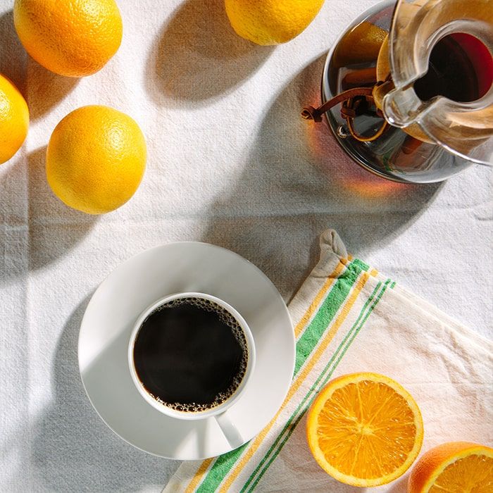 Coffee Bean Direct Decaf Seville Orange flavored coffee -- coffee mug on dish alongside glass pourover and various oranges