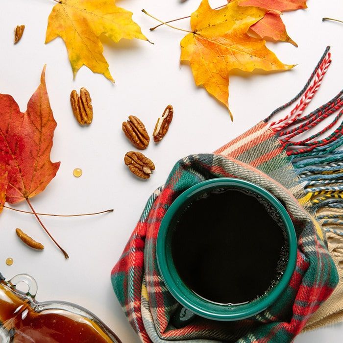 Coffee Bean Direct Vermont Maple Crunch flavored coffee -- colorful scarf wrapped around green coffee mug filled with coffee alongside scattered walnuts, jar of maple syrup, and colorful fall leaves